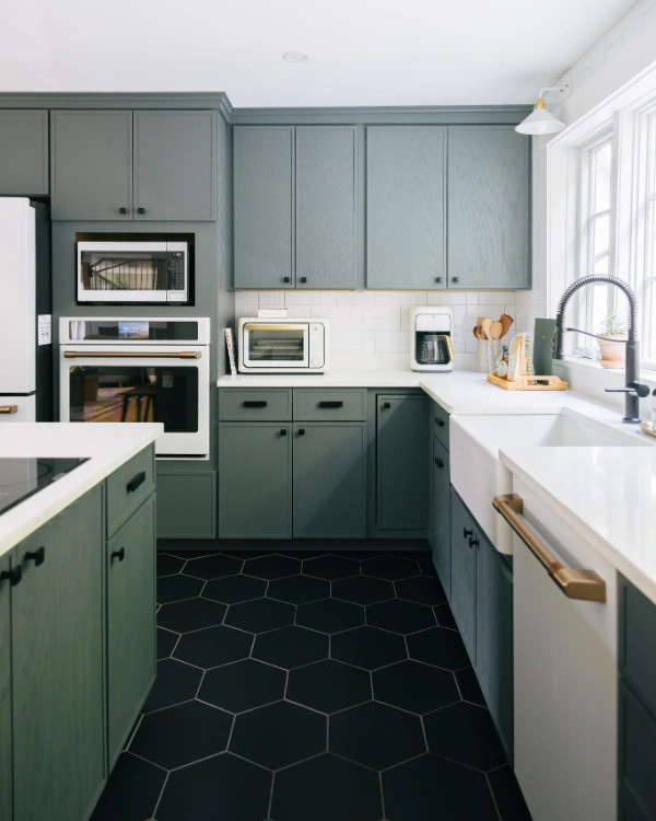 Modern kitchen workspace with built-in appliances, green shaker cabinets, white tile backsplash, and black hex tile flooring
